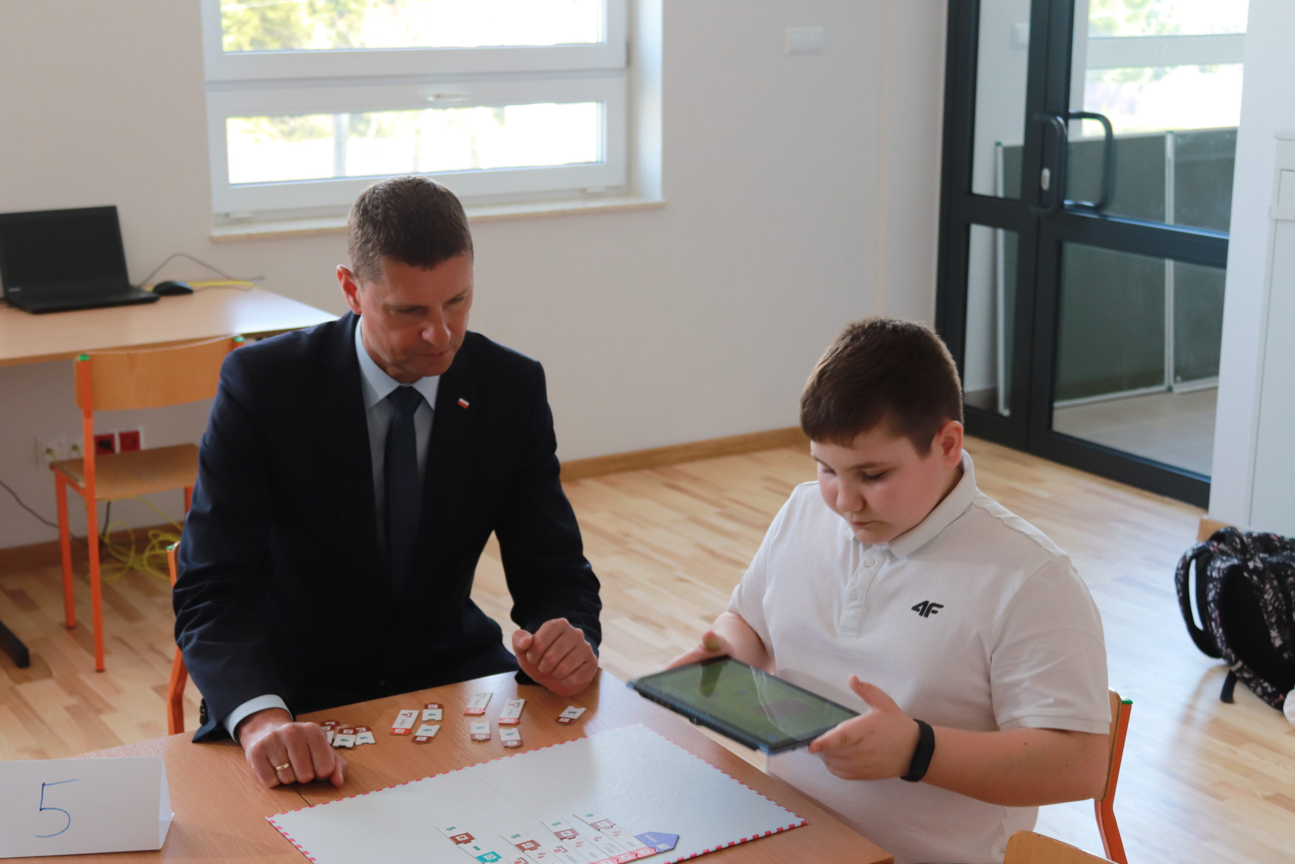 Na zdjęciu widoczny jest Pan Wiceminister edukacji i nauki Dariusz Piontkowski po prawej stronie siedzi uczeń trzymający tablet.