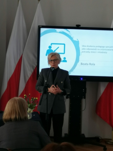 Beata Rola – pani Beata Rola na tle flag biało-czerwonych i monitora z tematem wykładu