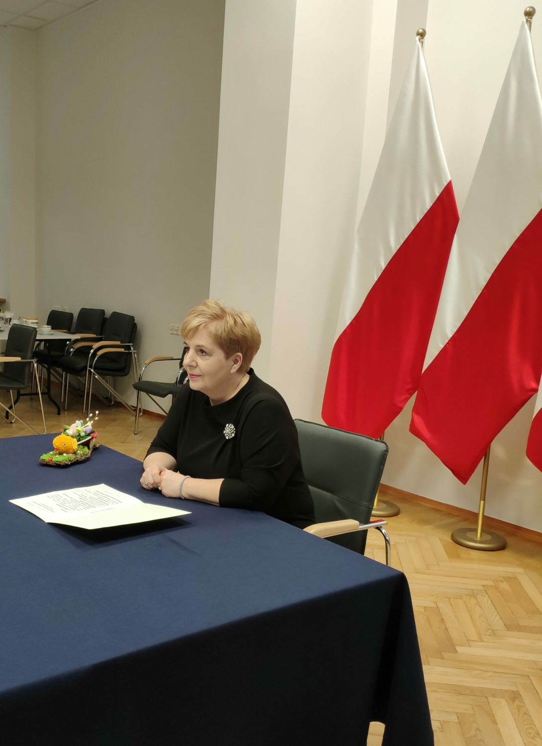 Pani Kurator Beata Pietruszka siedzi przy stole na tle flag biało-czerwonych.